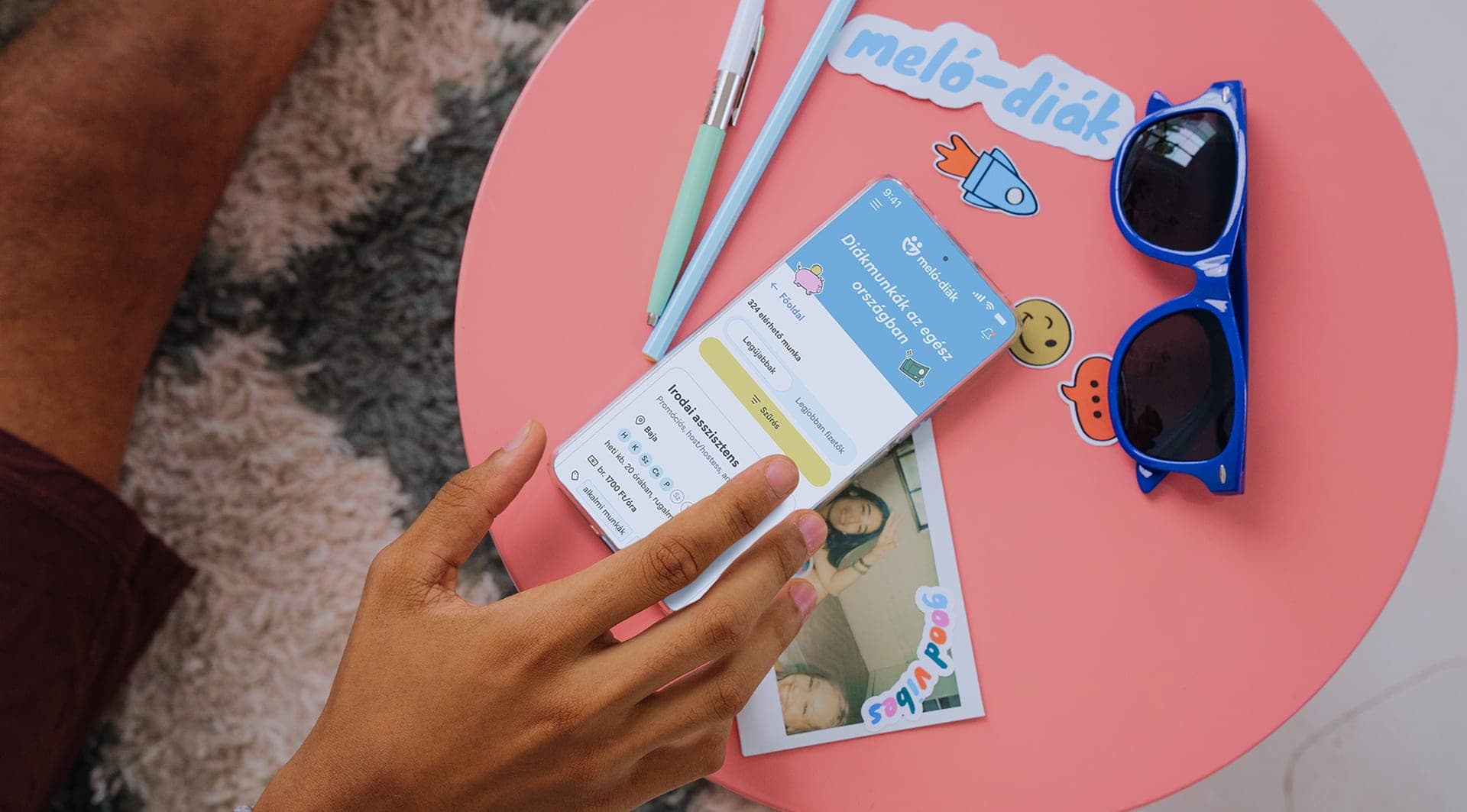 The Meló-Diák mobile app and stickers on a pink table